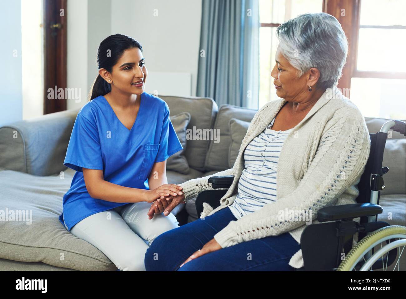 Continuate ad essere ottimisti e tutto andrà bene: Una donna anziana preoccupata seduta su una sedia a rotelle mentre un'infermiera tiene la mano Foto Stock