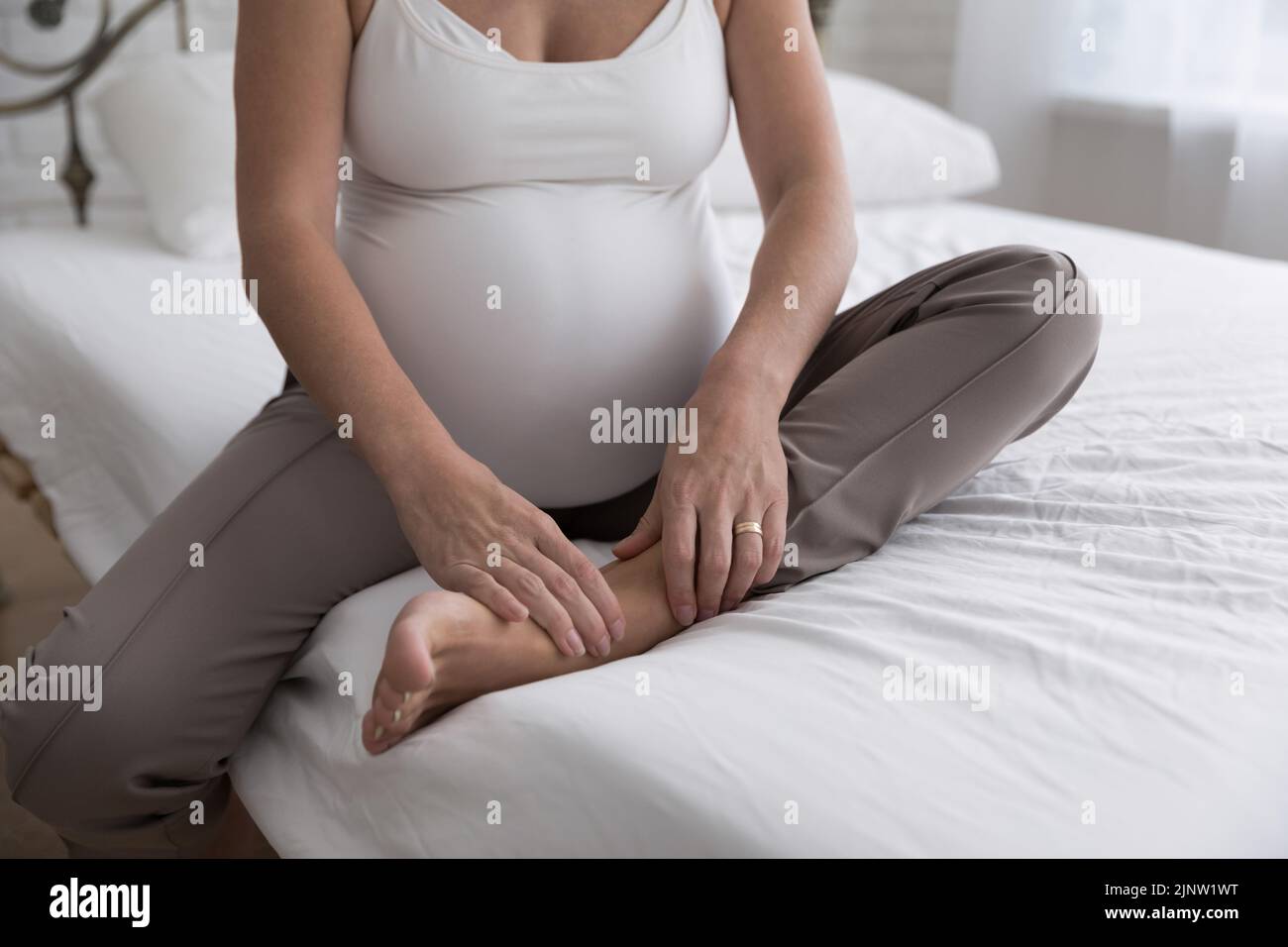 Donna incinta si siede sul letto toccare la sua caviglia dolorante Foto Stock