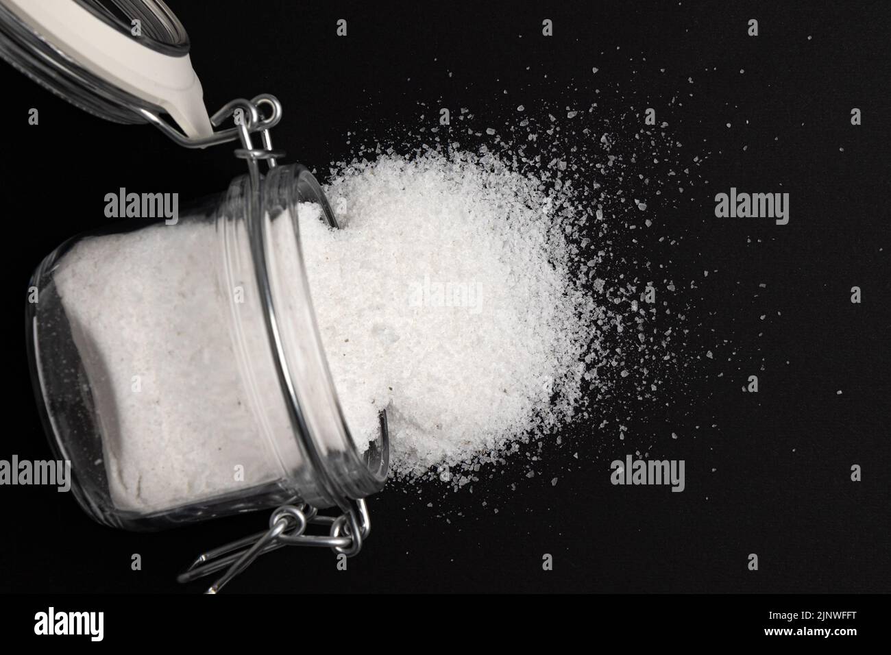 sale marino in vaso di vetro isolato su fondo nero, prodotto minerale utilizzato in cucina e cosmetici, macro foto di condimento, primo piano Foto Stock
