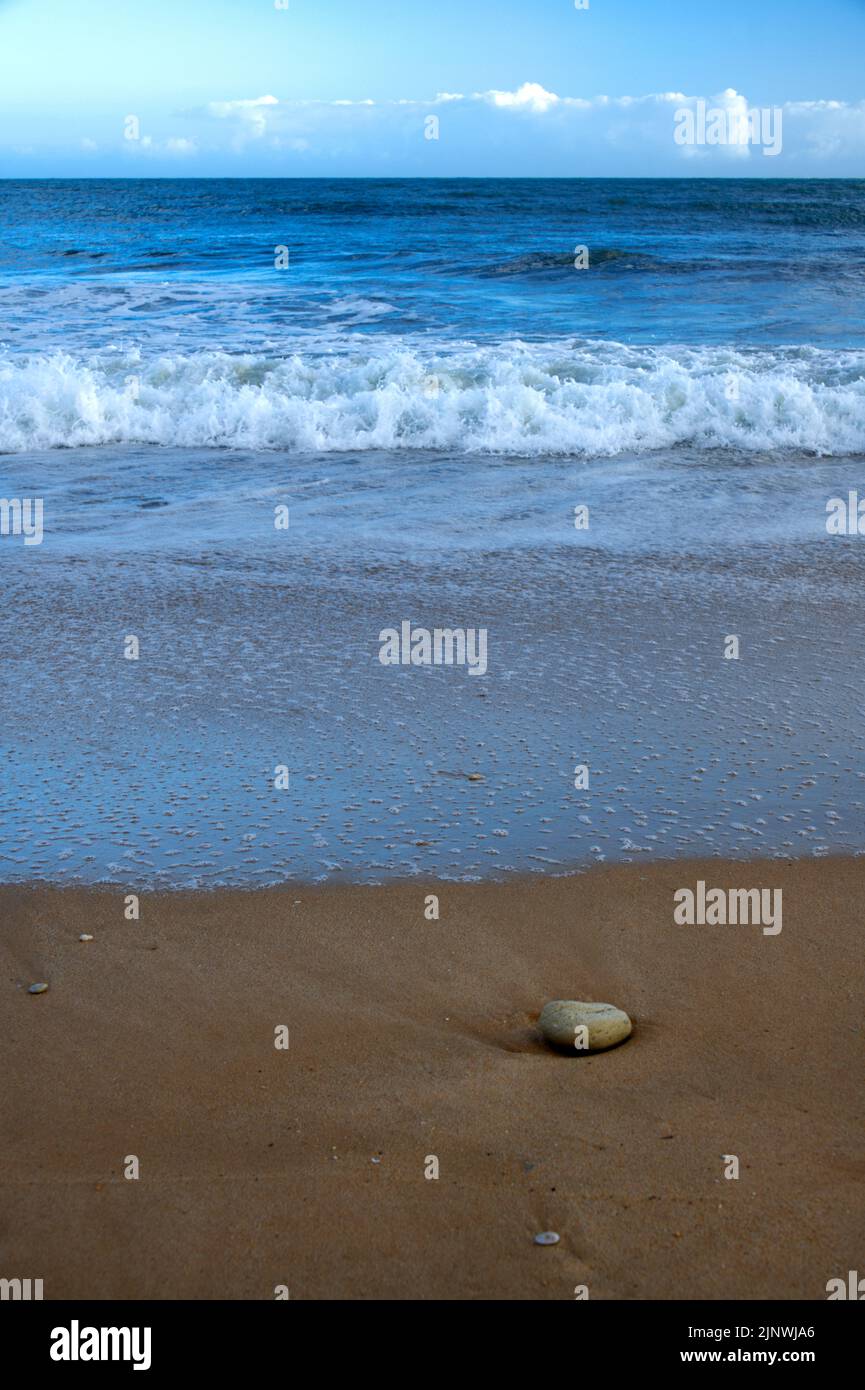 Piccola pietra sulla spiaggia contro il grande oceano e il cielo nuvoloso blu Foto Stock