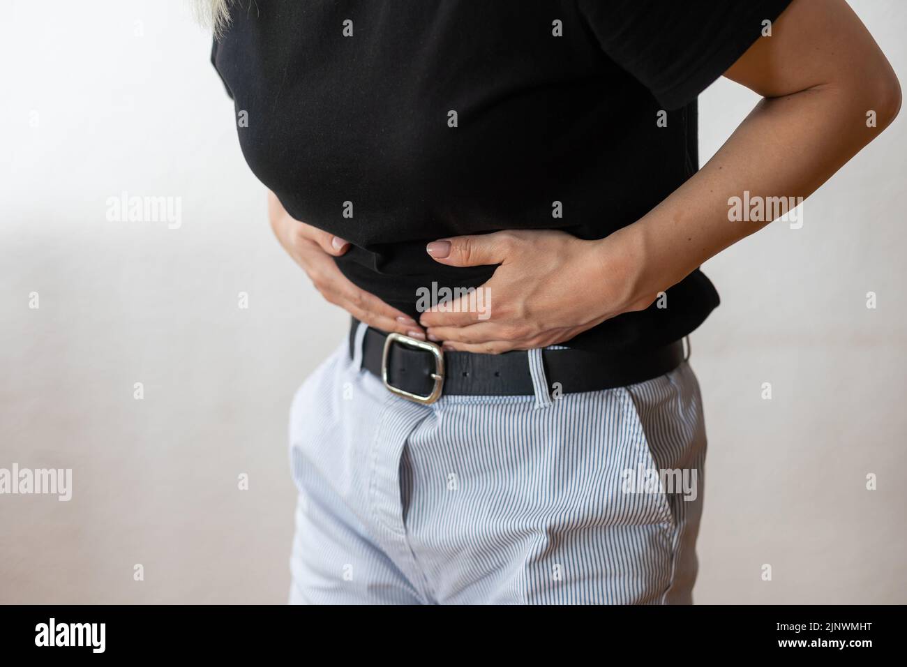 Una donna in piedi davanti a uno sfondo bianco e tenendo le mani sul ventre. Foto Stock