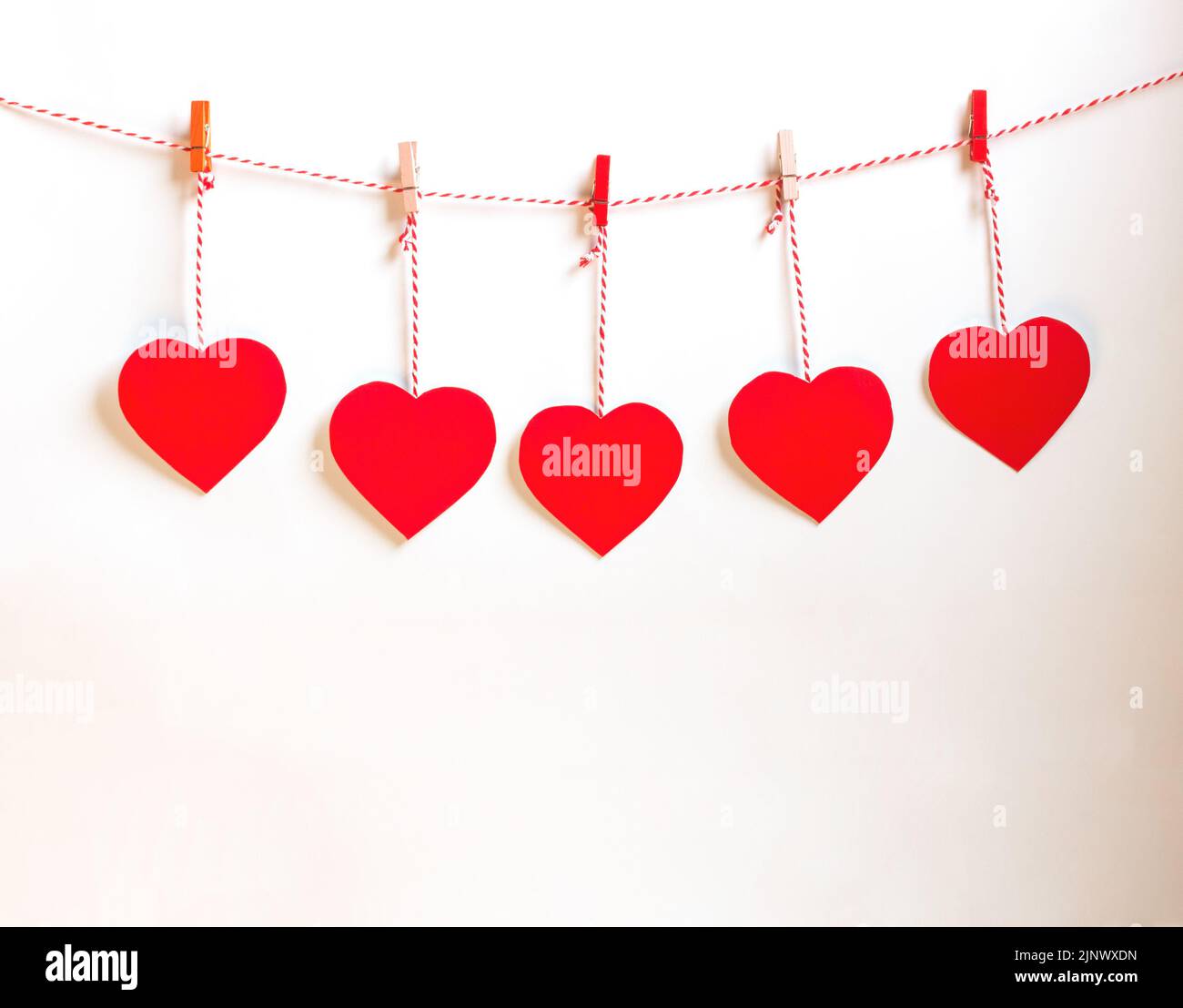 Carta cuore rosso tagliata con cordoncino naturale e clip rosse appesi su sfondo bianco, copia spazio, San Valentino - immagine Foto Stock