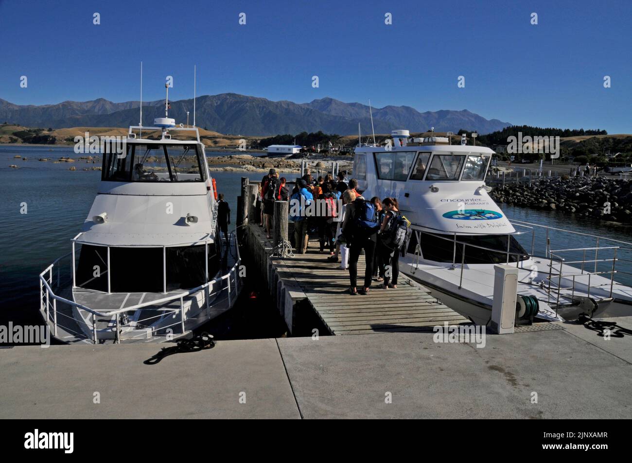 I turisti si riuniscono sulla banchina in attesa di salire a bordo delle due barche per l'osservazione dei delfini vicino alla città di Kaikoura sulla costa orientale dell'Isola del Sud in Nuova Zelanda. Foto Stock