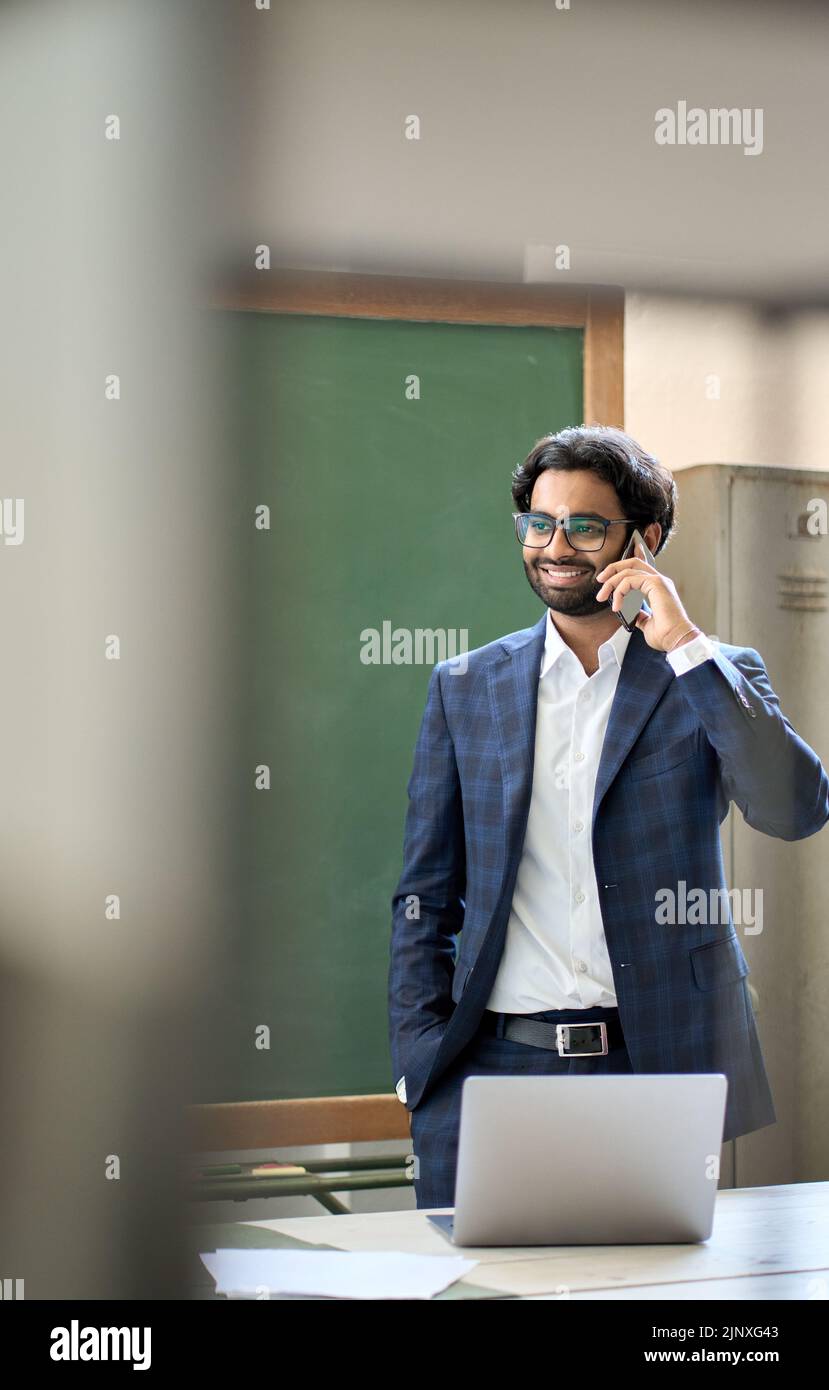 Giovane uomo d'affari indiano sorridente che indossa il vestito che parla al telefono sul posto di lavoro. Foto Stock