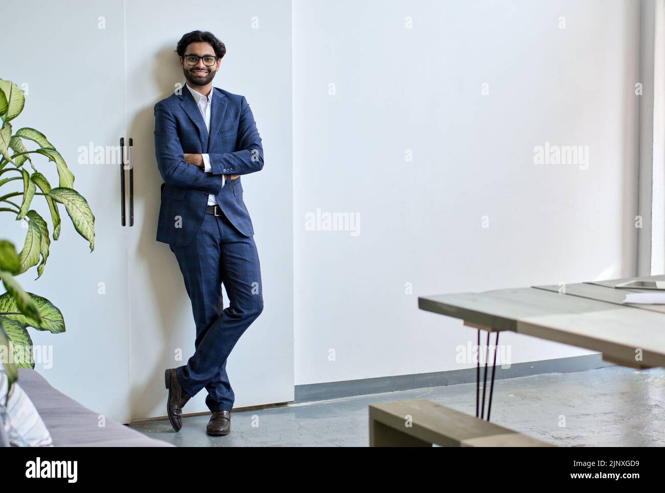 Sorridente giovane uomo indiano d'affari indossa tuta stand in ufficio, ritratto. Foto Stock