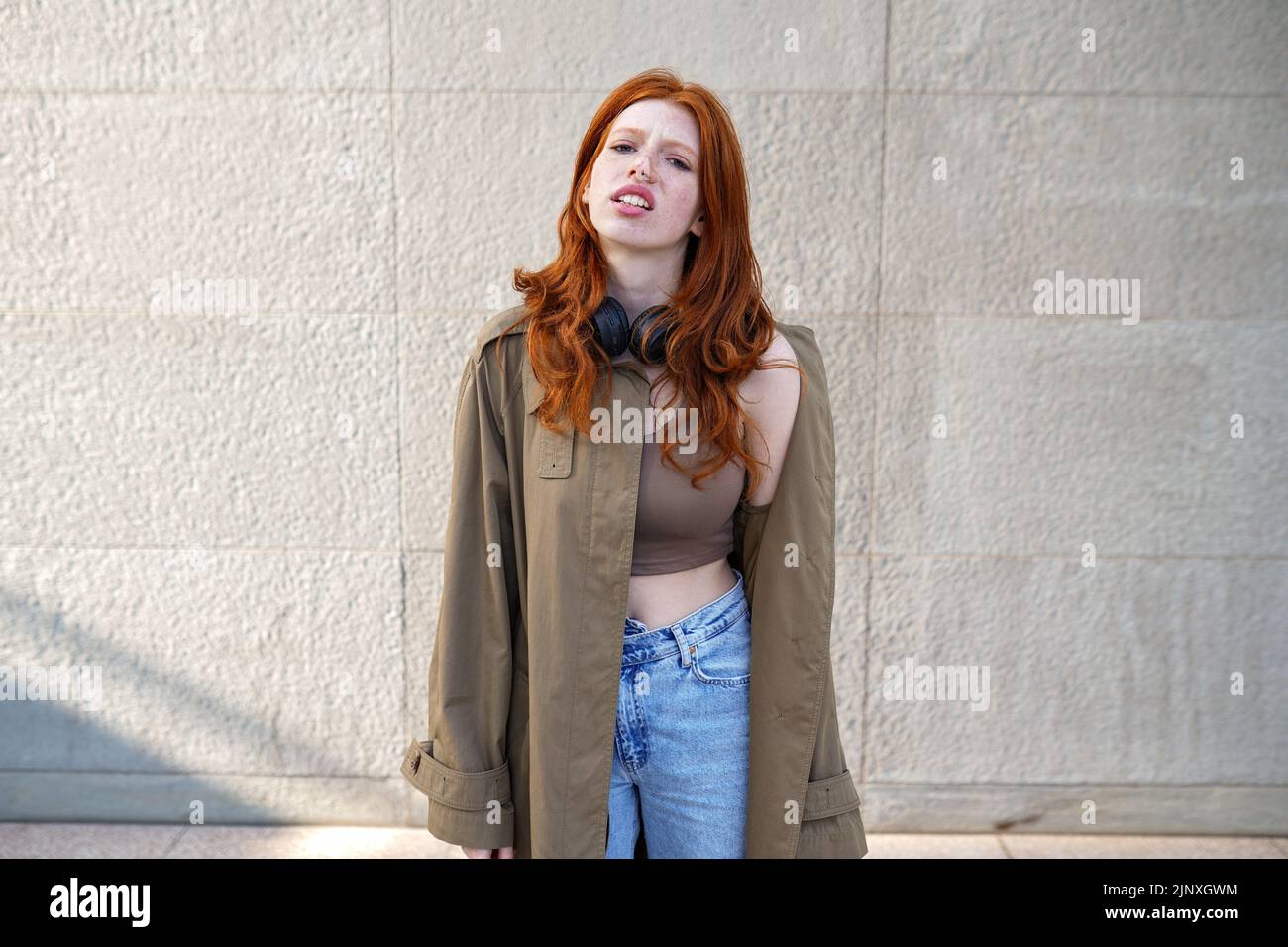 Ragazza Hipster Redhead in piedi su sfondo muro urbano cercando annoiato. Foto Stock