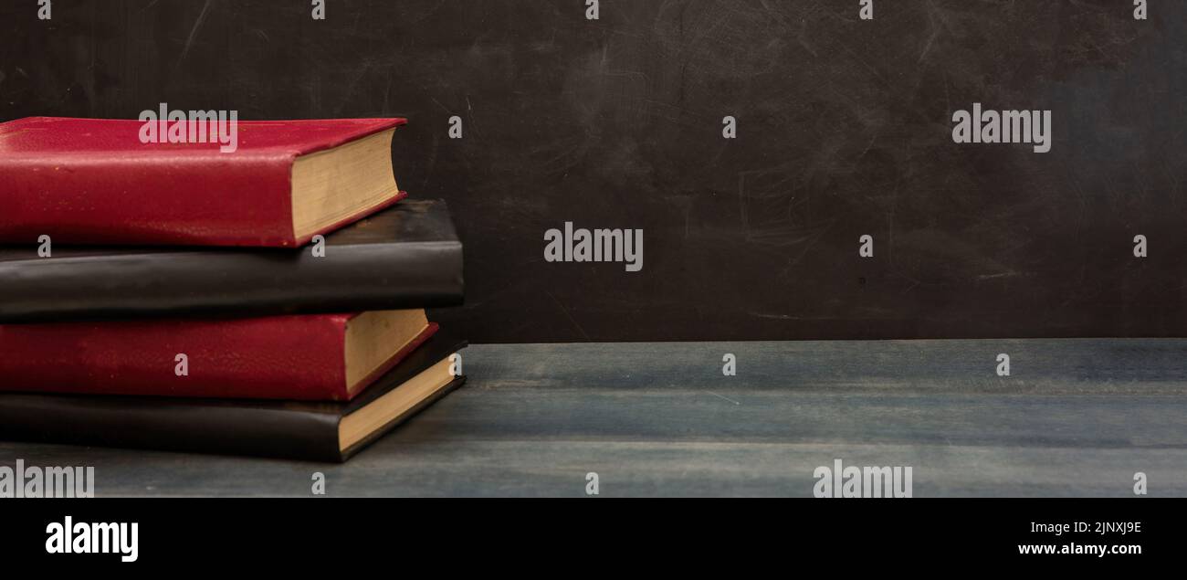 Torna al modello scolastico. I libri si impilano su un tavolo di legno blu della classe, sfondo nero vuoto, spazio per la copia Foto Stock