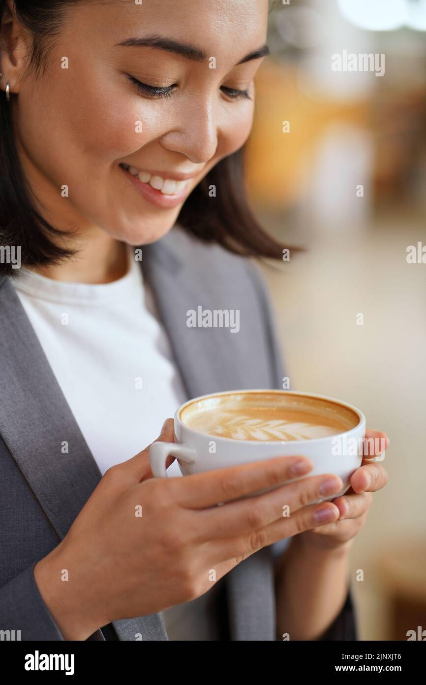 Giovane donna asiatica sorridente che tiene la tazza che beve il latte del caffè godendo l'aroma. Foto Stock