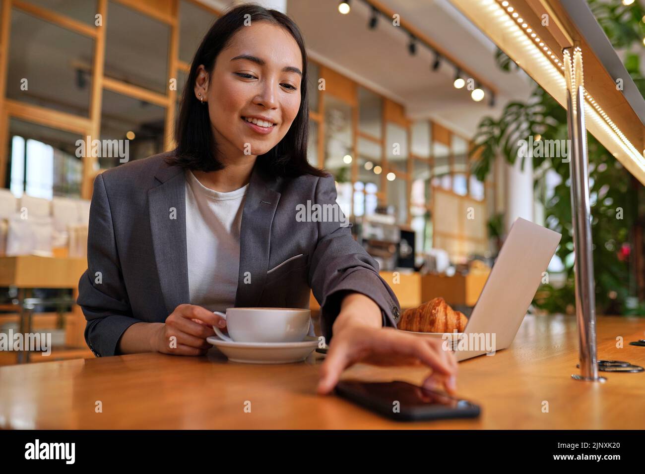 Felice donna asiatica d'affari vestito bere caffè utilizzando il telefono in caffetteria. Foto Stock