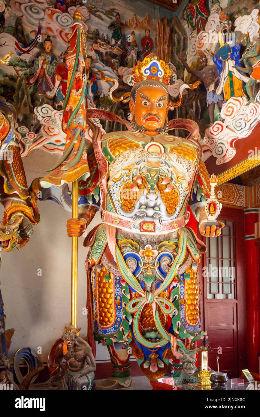 Primo piano di una statua o scultura religiosa cinese all'interno di un tempio. Il simbolo ha un abbigliamento multicolore e sta tenendo un banner Foto Stock