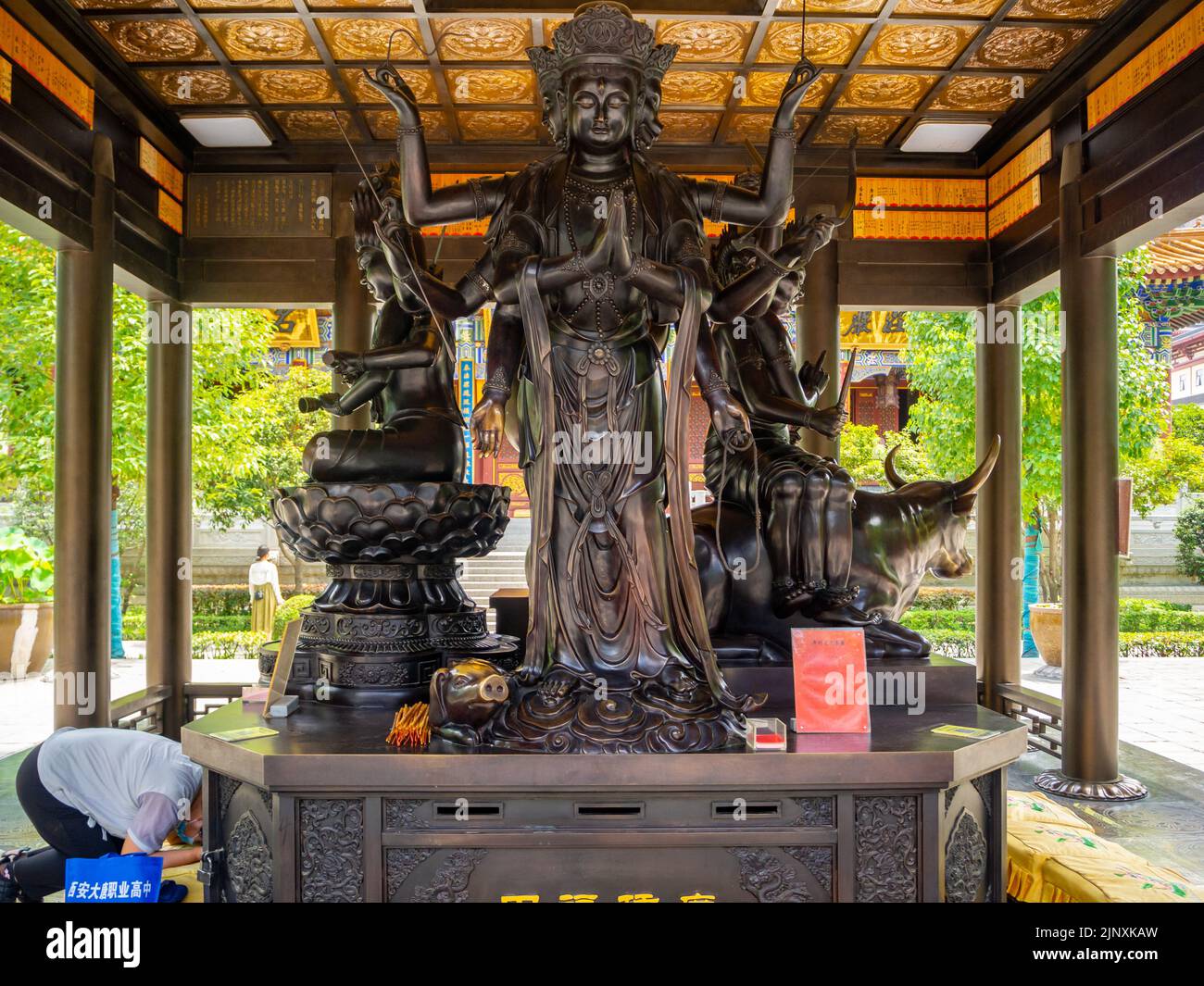 Un uomo prega per una scultura o una statua religiosa tradizionale che si trova sotto un gazebo in un parco pubblico. Il simbolo fa parte del cu. Cinese Foto Stock