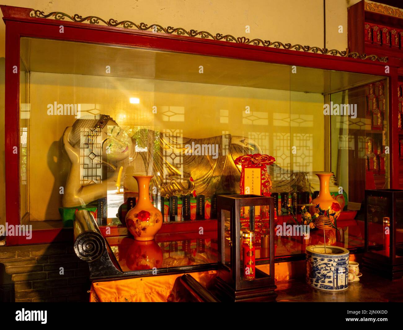 La statua dorata o la scultura di una donna sdraiata si trova dietro un'urna di vetro all'interno di un tempio tradizionale cinese. Foto Stock