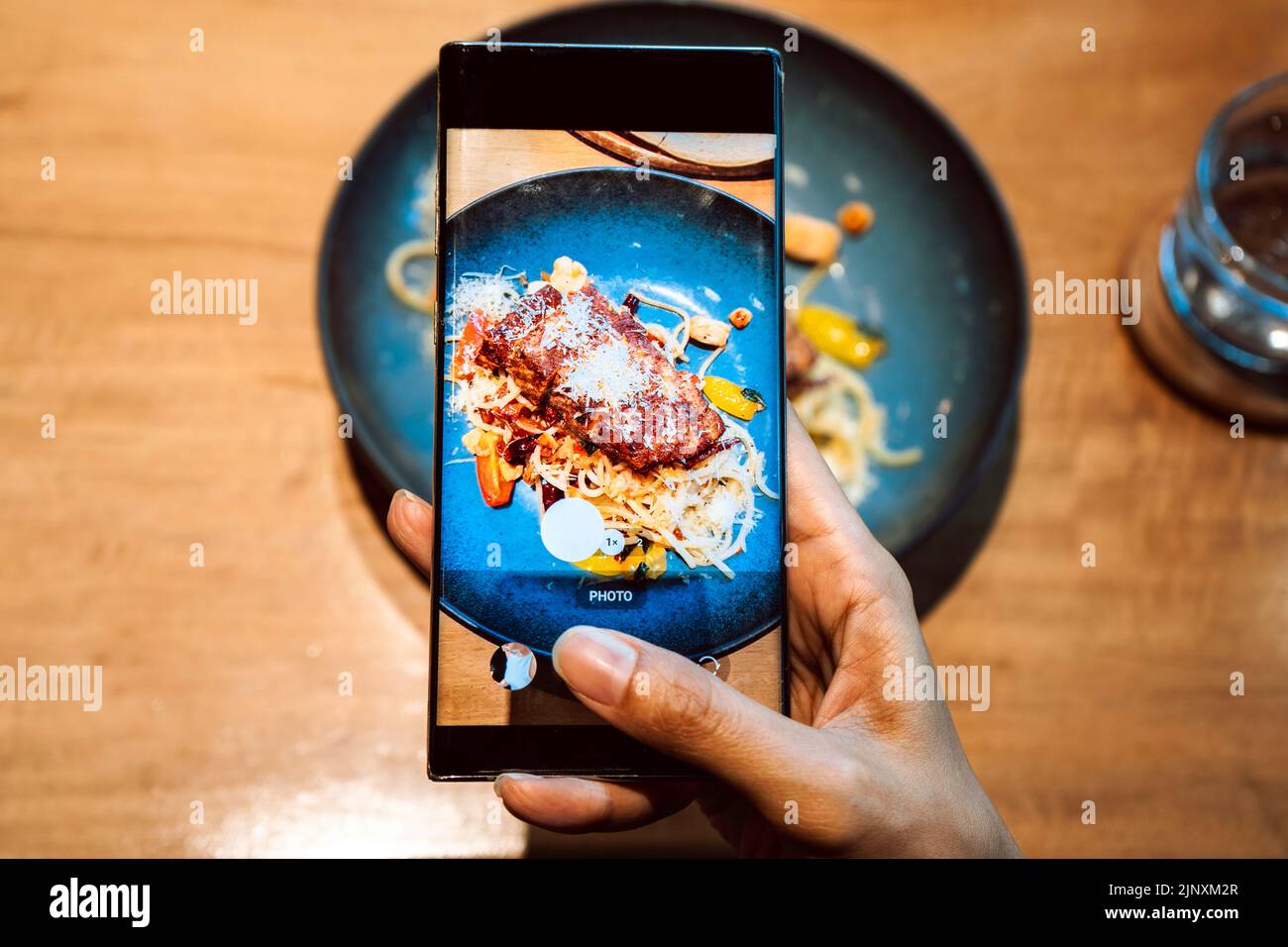 Primo piano di mano di una donna che scatta una foto di cibo con il telefono cellulare. Condivisione sui social media Foto Stock