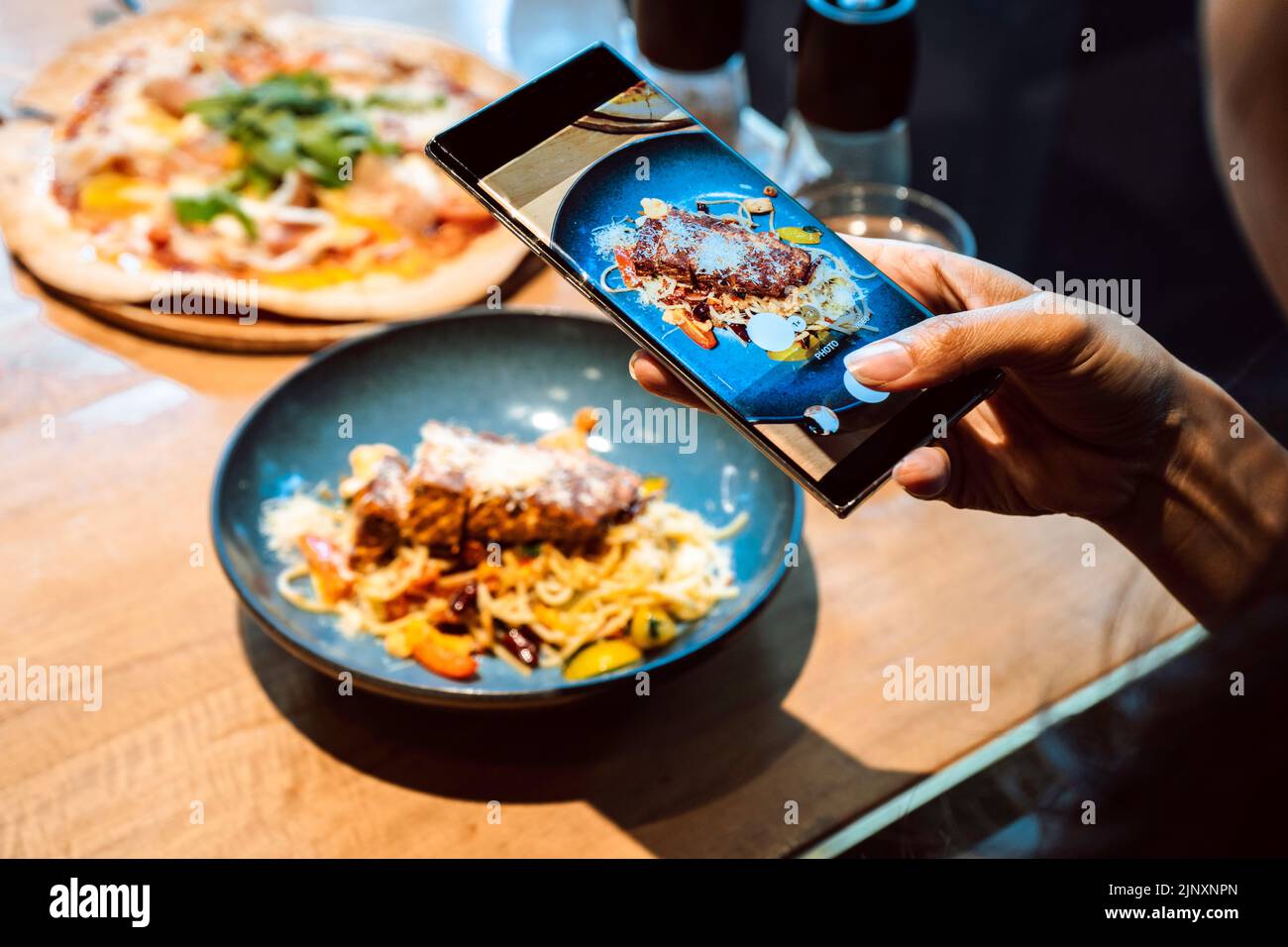 Primo piano di mano di una donna che scatta una foto di cibo con il telefono cellulare. Condivisione sui social media Foto Stock