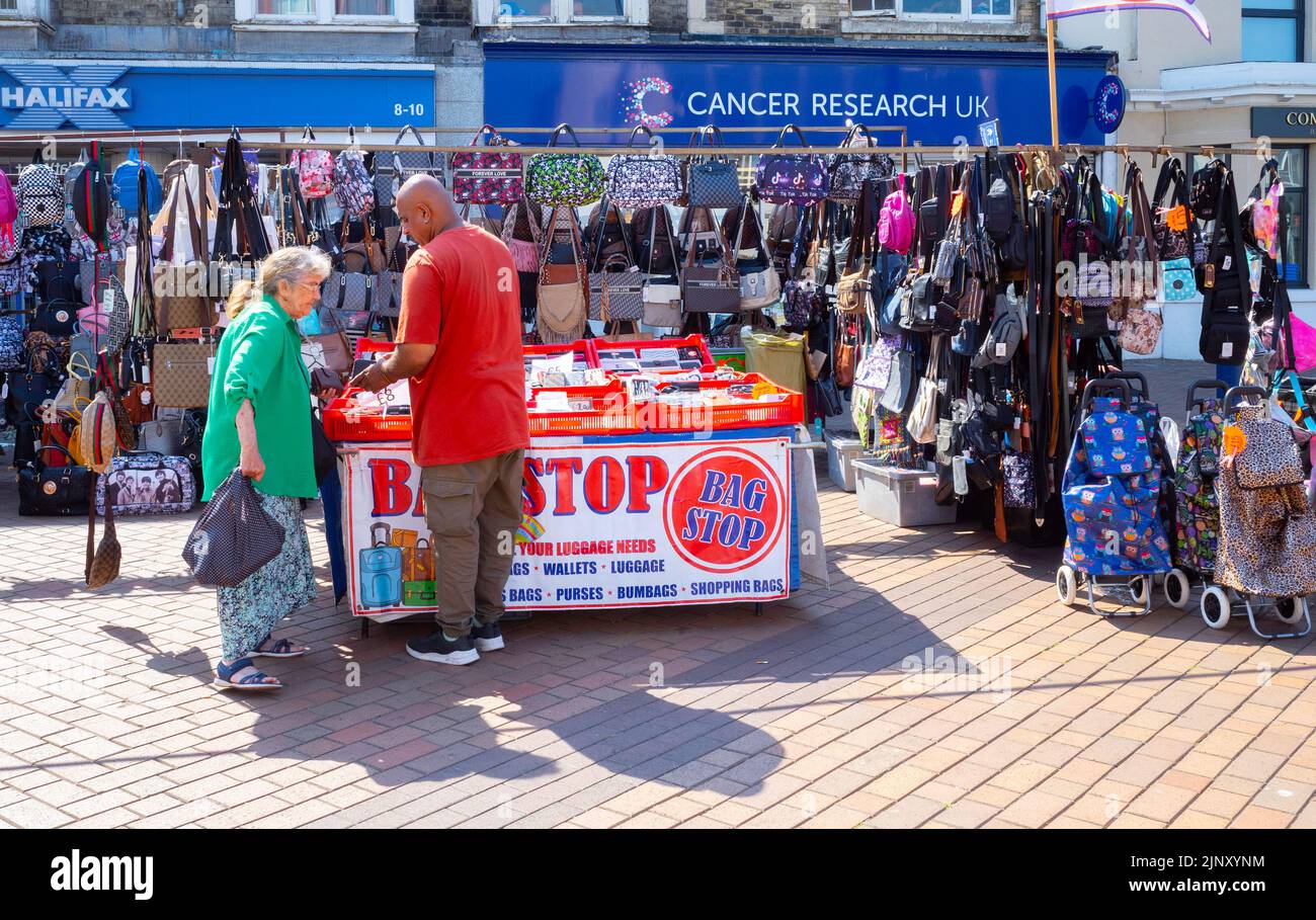 Borsa Stop uomo alla sua stalla vendere una borsa a una signora cliente, con tutti i tipi di borse e portafogli bagagli su una stalla settimanale mercato Redcar Hig Foto Stock