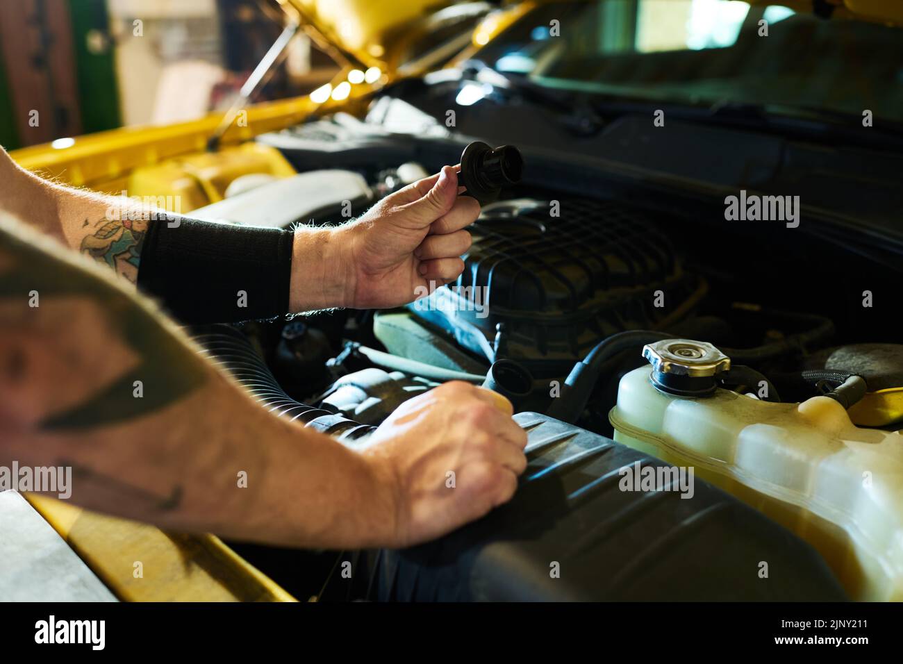 Mani di un giovane uomo che tiene il dettaglio del motore dell'automobile sopra il cofano aperto mentre controlla il motore e sceglie le parti di ricambio adatte prima della riparazione Foto Stock