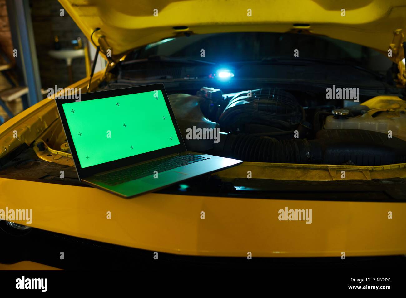 Computer portatile con schermo verde in piedi sul motore di auto elettrica di colore giallo con cofano aperto prima o durante il controllo tecnico Foto Stock