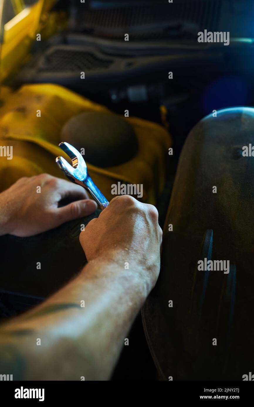 Mani di giovane tecnico muscolare o riparatore con chiave metallica in piedi davanti al motore di auto mentre andando a riparare i suoi dettagli Foto Stock