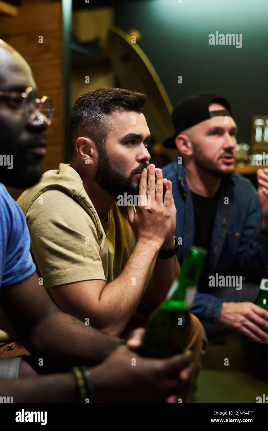 Giovane uomo che tiene le mani messe insieme dal viso, mentre esprime ansia per la squadra di calcio preferita durante la trasmissione della partita Foto Stock