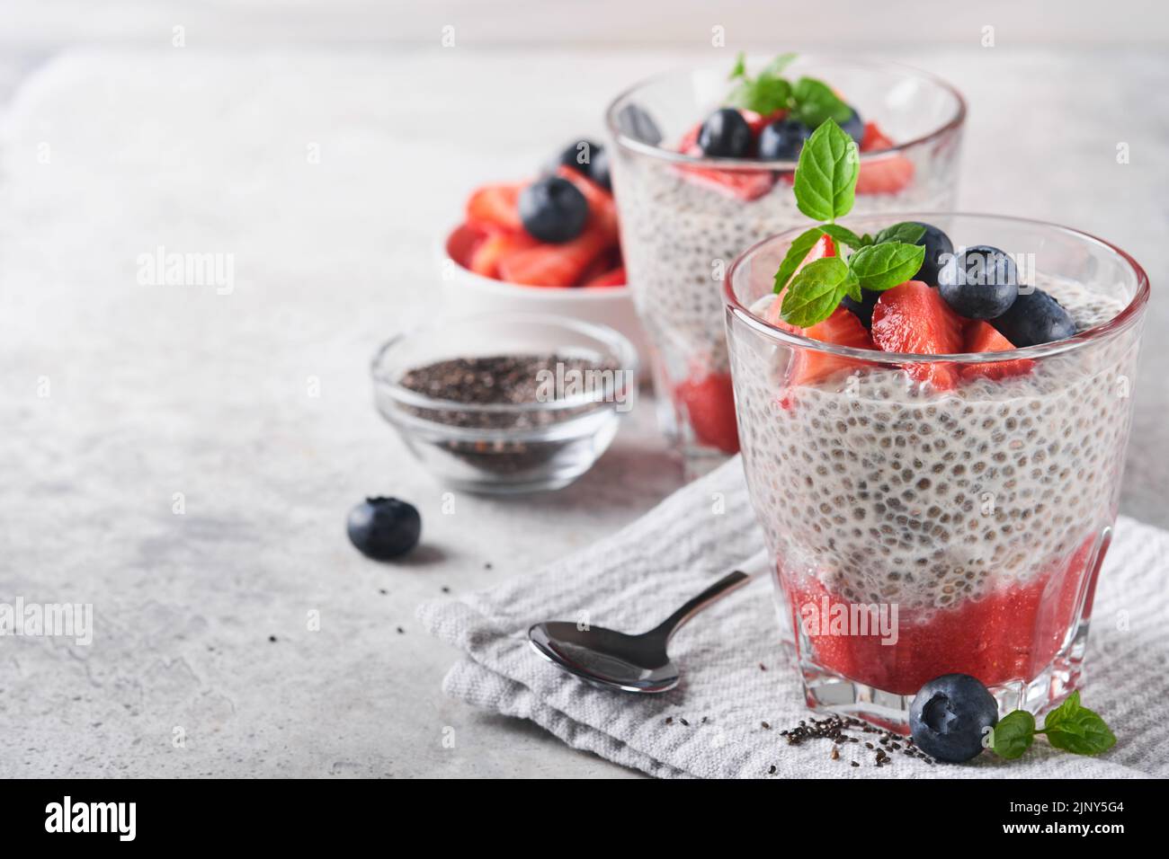 Budino di fragole Chia. Sana colazione vegana pudding di semi di chia con bacche fresche e menta in vetro su sfondo di cemento grigio. Concetto di healt Foto Stock