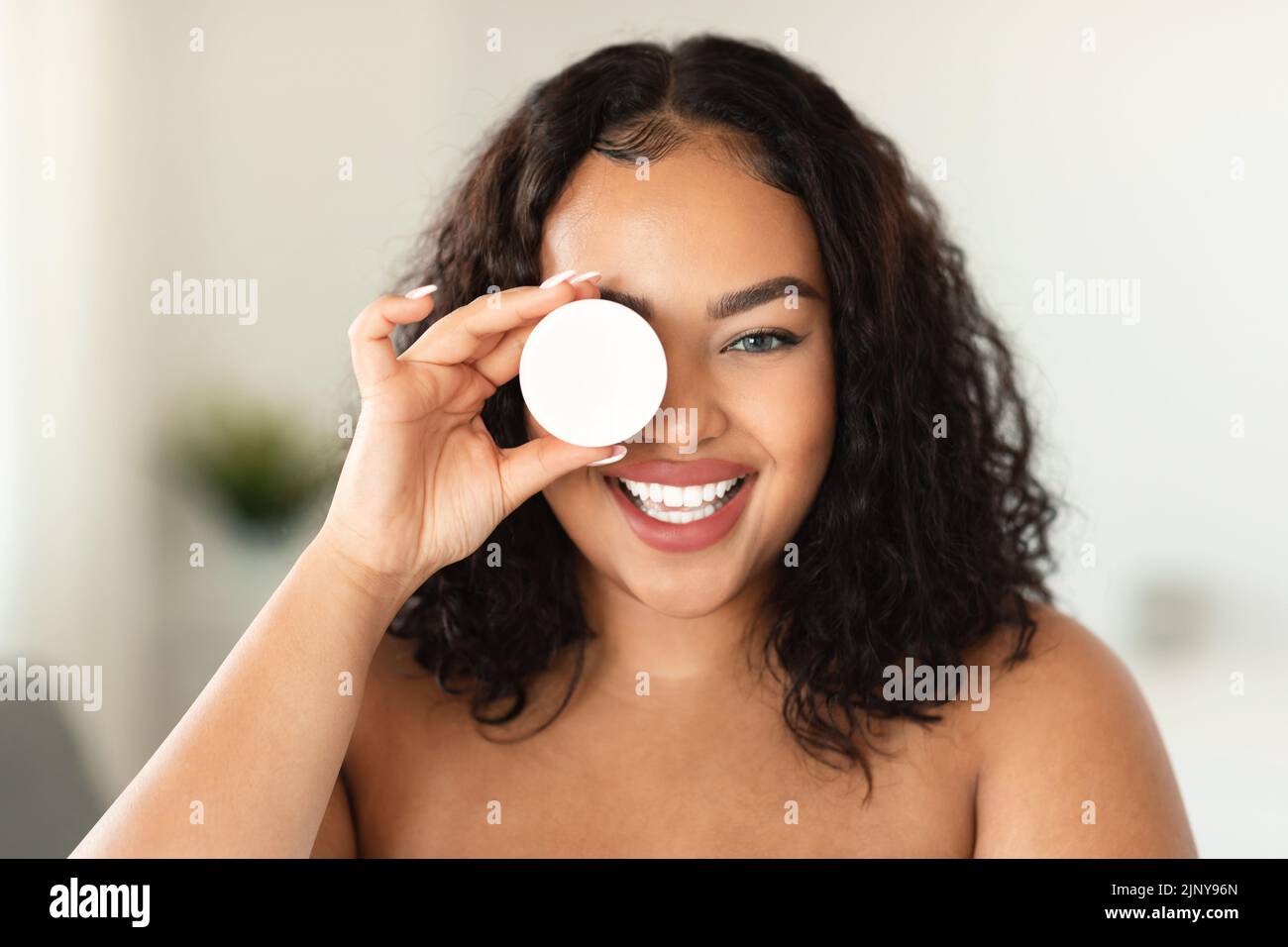 Prodotti di bellezza. Barattolo da donna nero emozionato con crema nutriente, che copre un occhio con un articolo per la cura della pelle Foto Stock