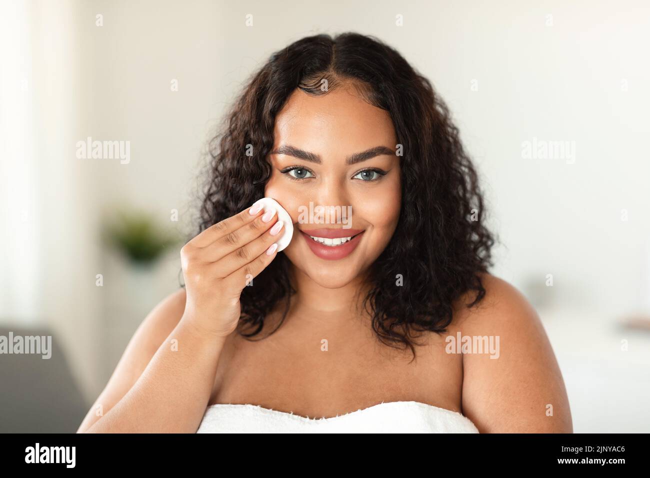 Concetto di cura della pelle. Buon nero sovrappeso donna pulizia viso con tampone di cotone, rendendo auto-cura di bellezza routine Foto Stock