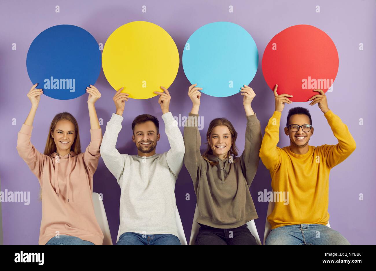 Giovani persone multirazziali seduti in fila e tenendo colorate bolle di discorso rotondo con spazio copia. Foto Stock