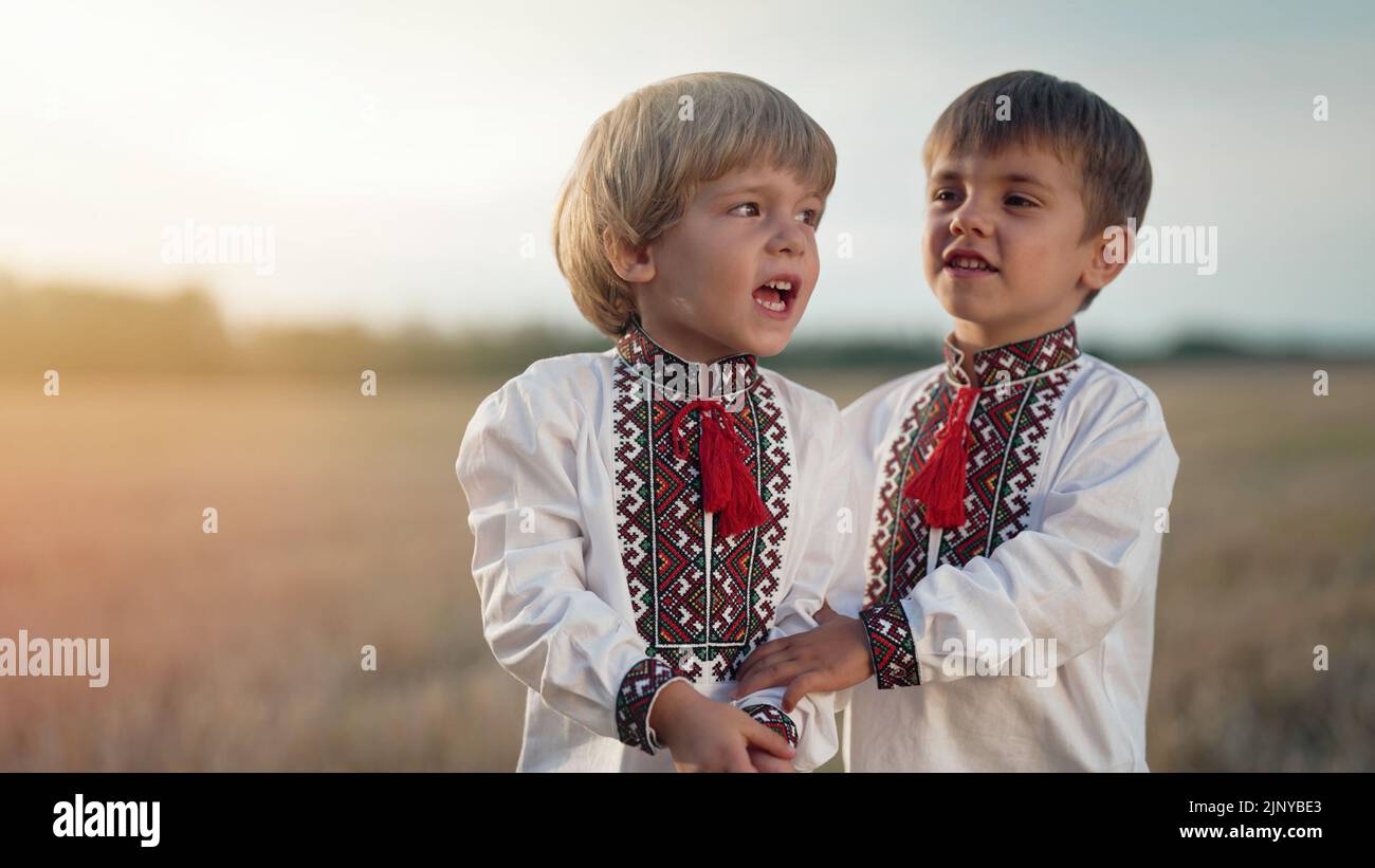 Bel ritratto di piccoli ragazzi ucraini cantando canzone in campo di grano dopo la raccolta. Bambini in maglia vyshyvanka ricamata tradizionale. Ucraina Foto Stock