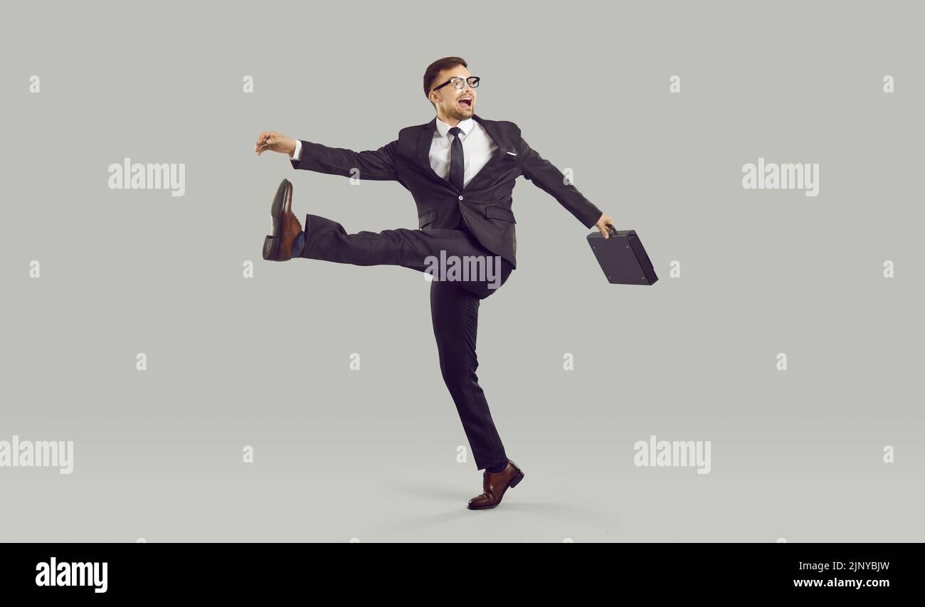 Uomo d'affari con impazzita espressione facciale che cammina stranamente, isolato su sfondo grigio. Foto Stock