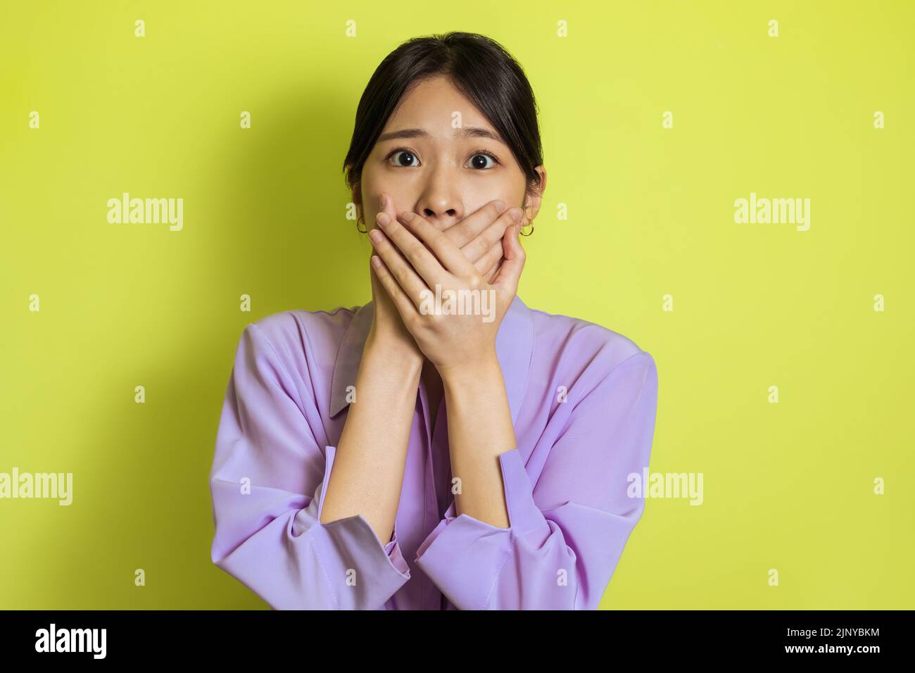 Scioccato giapponese femmina che copre la bocca guardando la macchina fotografica, sfondo giallo Foto Stock