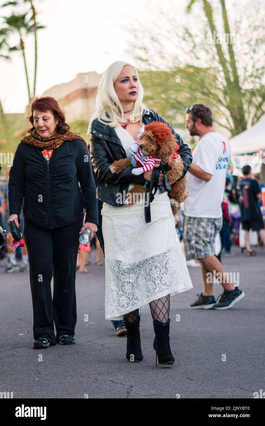 Donna bionda che tiene un barbotto marrone che indossa un costume mortale della bambola del cane ad una festa di Halloween a Fountain Hills, Arizona, Stati Uniti. Foto Stock