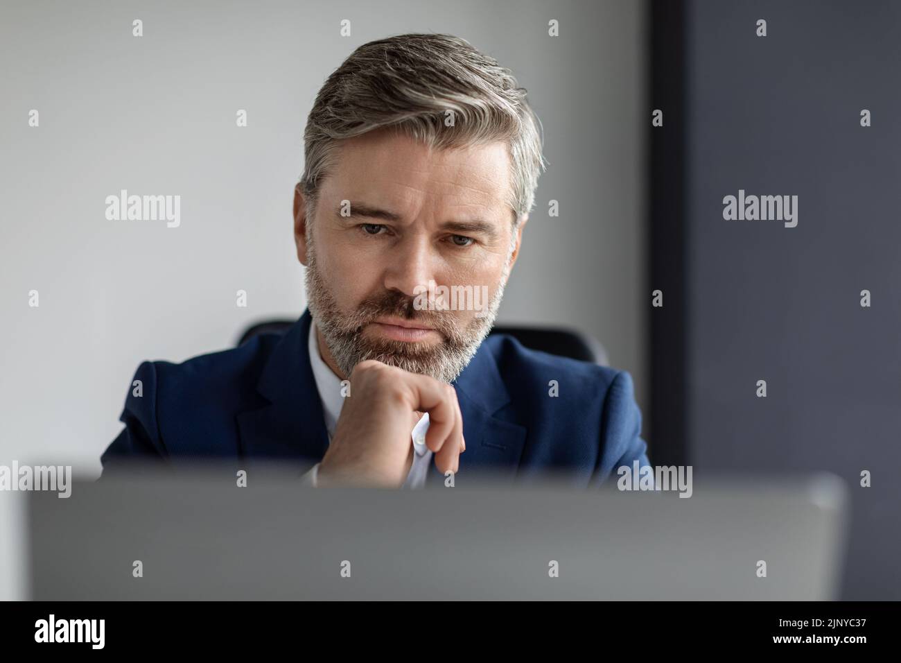 Ritratto di un uomo d'affari di mezza età che guarda lo schermo del notebook in ufficio Foto Stock