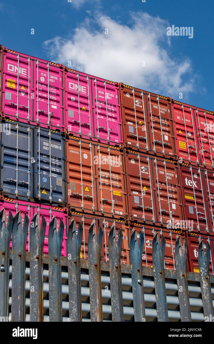 contenitori di spedizione impilati in un deposito nei moli a southampton nel regno unito, la spedizione contiene verniciato una varietà di colori luminosi carico. Foto Stock
