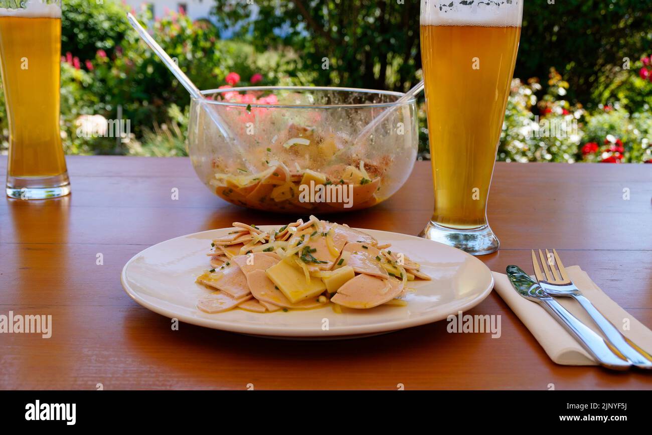 Una tradizionale, rustica e sostanziosa cena tedesca in una birreria all'aperto con un paio di birre, un'insalata di salsiccia svizzera (Wurstsalat) con formaggio e cipolle Foto Stock