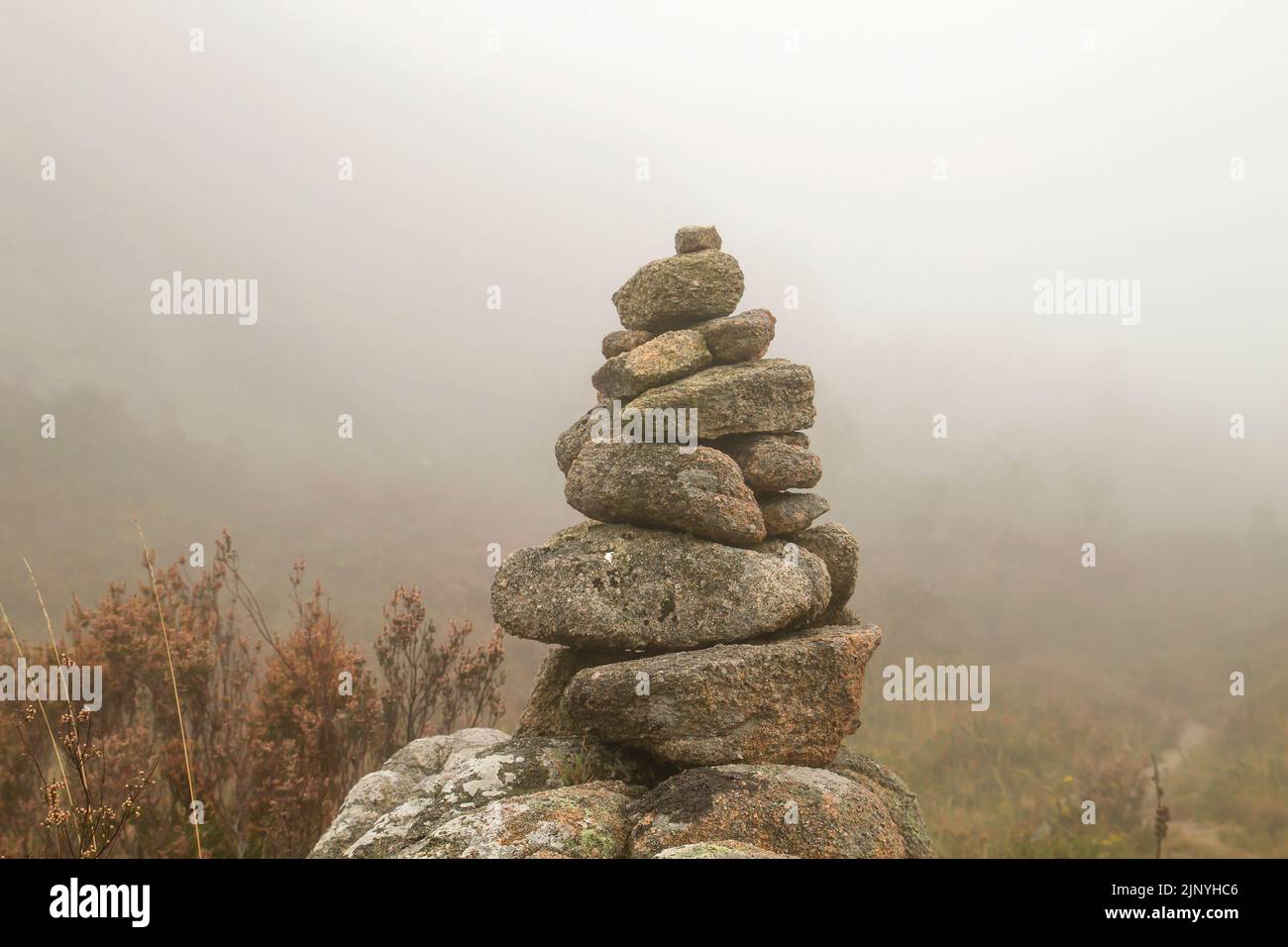 Cairn o marcatore in pietra in sentiero di montagna con nebbia e scarsa visibilità Foto Stock