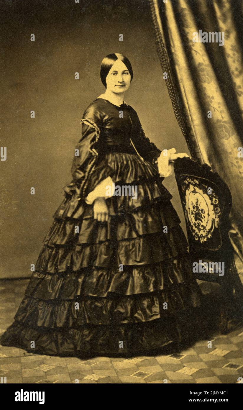 Fine 19th ° secolo Photo Studio Ritratto di formale donna seria in piedi in abiti d'epoca elegante con sfondo circa 1870 - 1880s Foto Stock