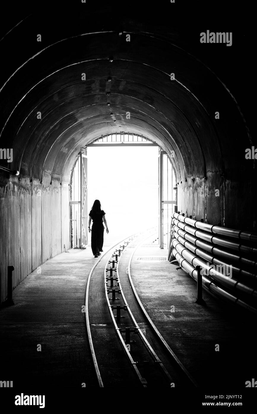 Silhouette di una giovane donna che esce da un tunnel scuro e si porta in una luce brillante. Foto Stock