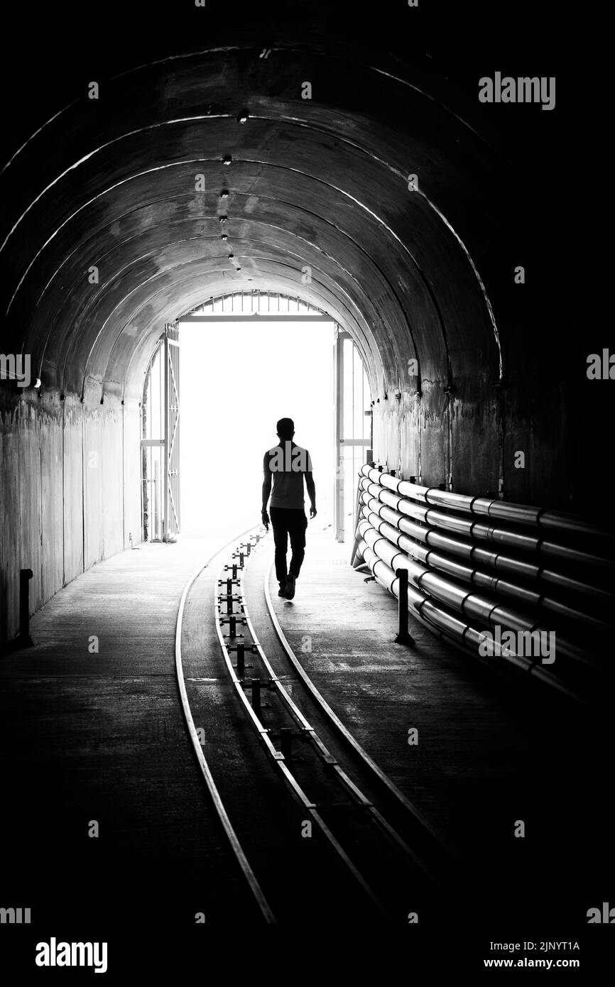 Silhouette di un giovane uomo che esce da un tunnel scuro e si porta in una luce brillante. Foto Stock