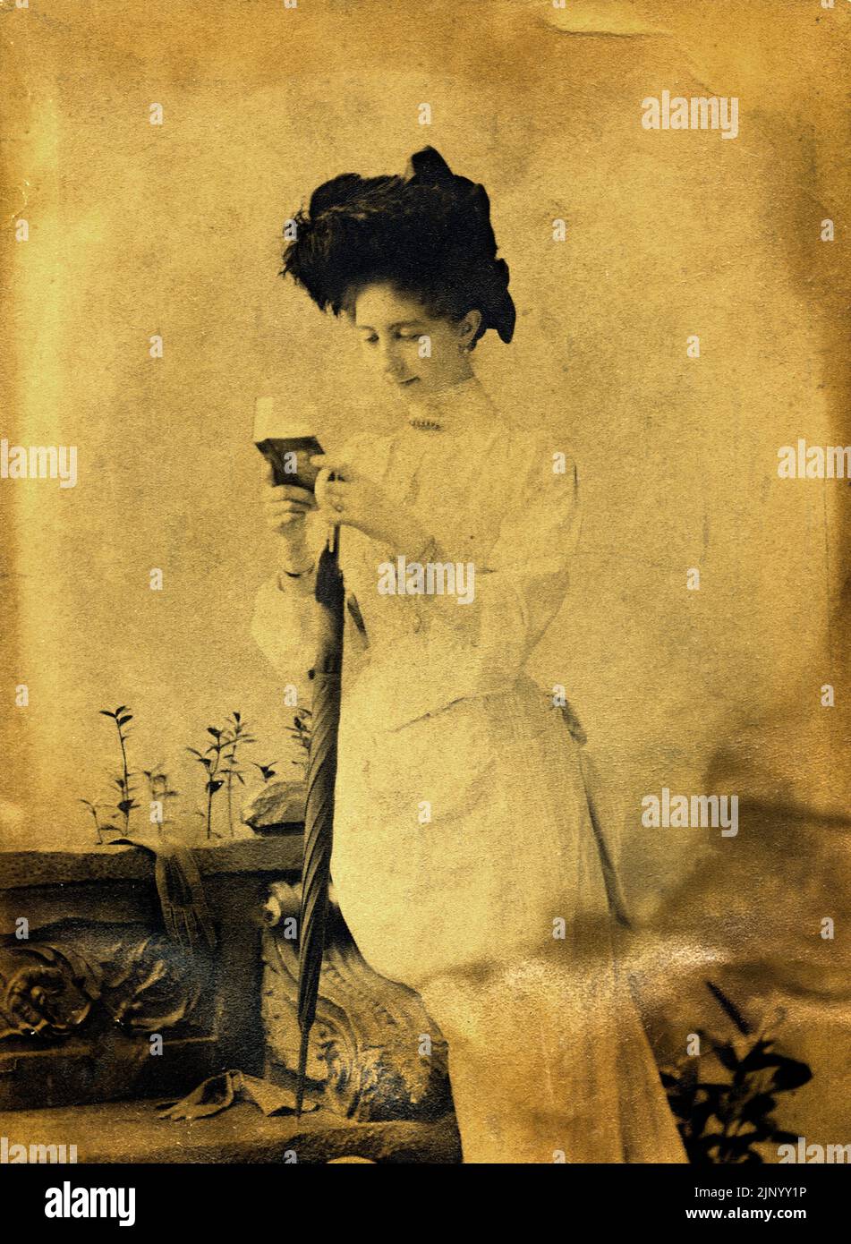 Fotografia vintage scattata in studio ritratto nel tardo 19th ° secolo di giovane donna seduto in abiti d'epoca lettura di un libro e tenendo un ombrello mentre in posa per la fotocamera circa 1889 - Budapest Foto Stock