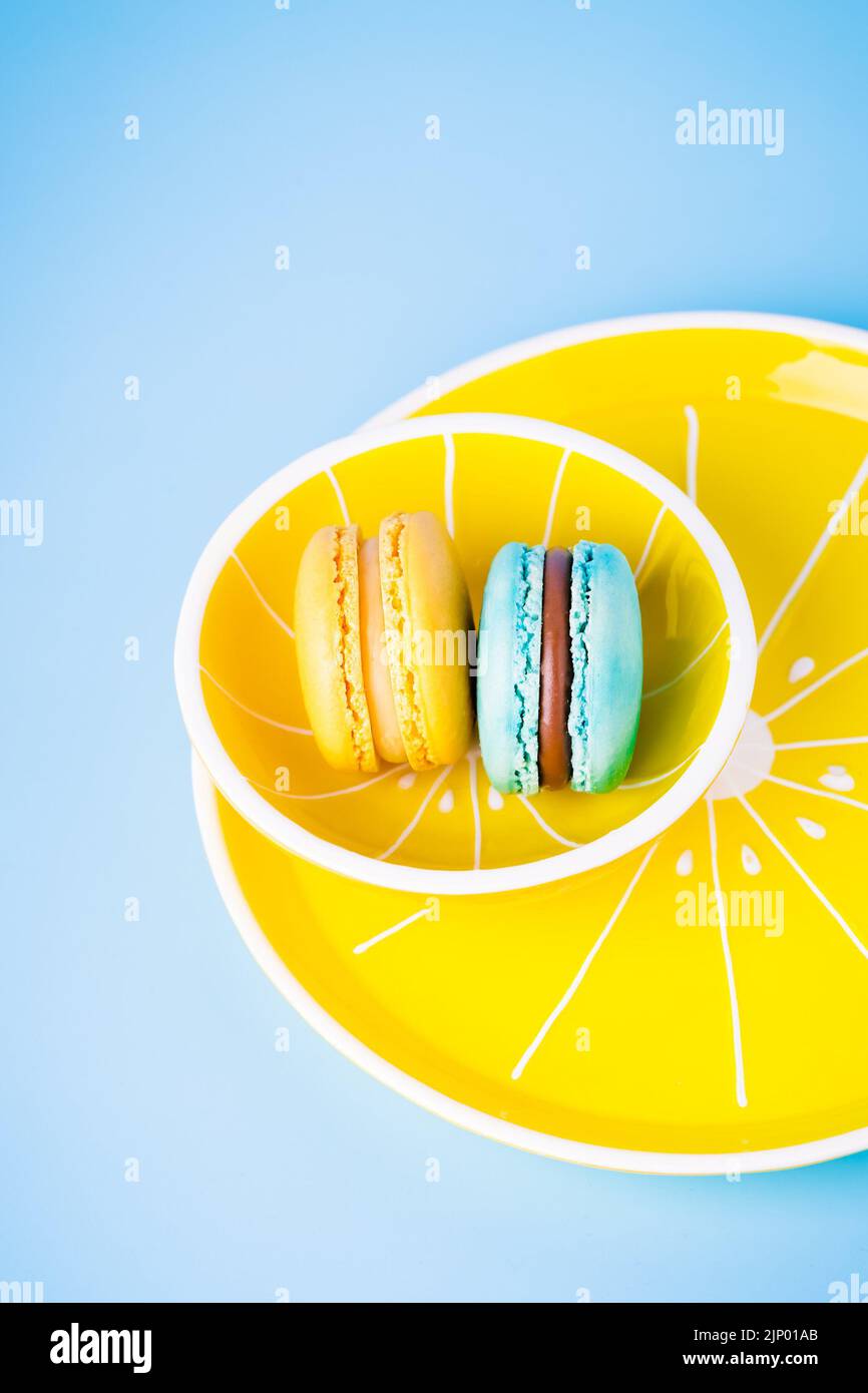 Macaron blu e giallo su piatto giallo e fondo blu Foto Stock