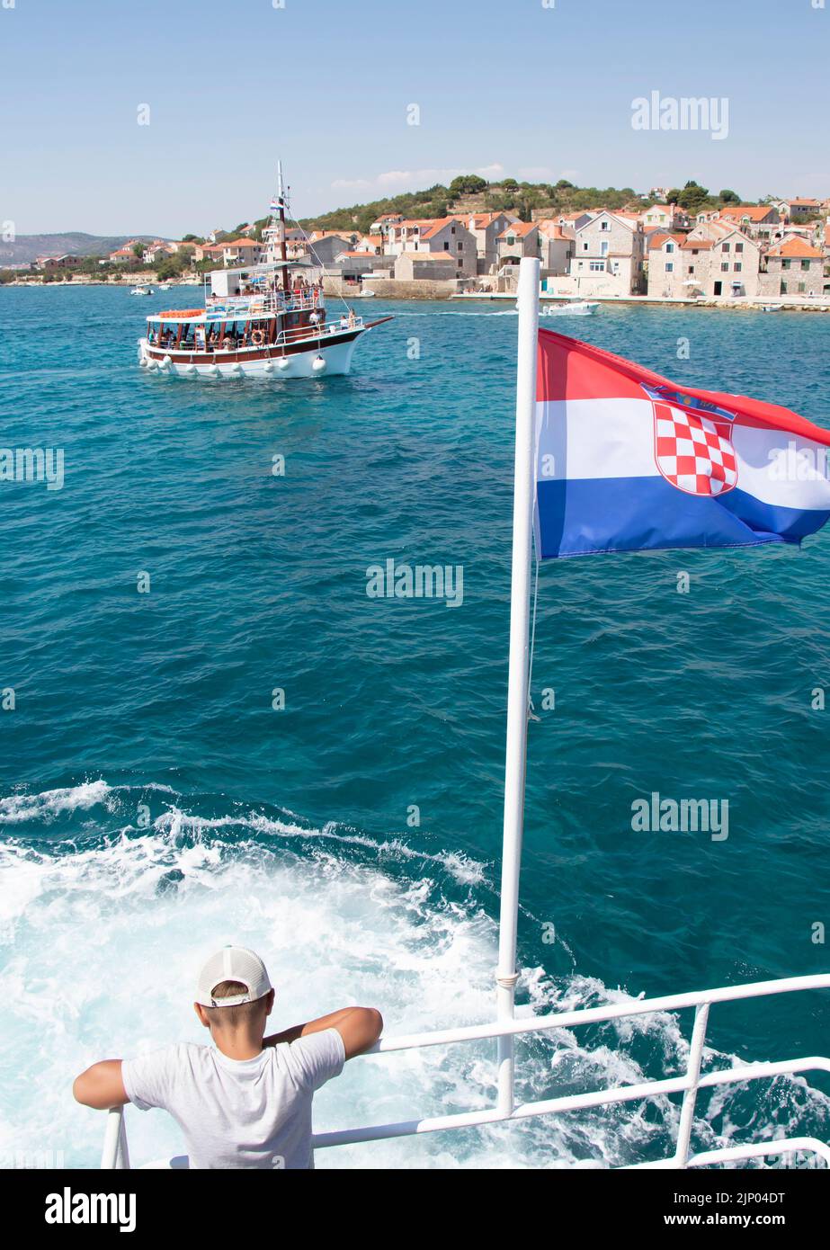 Isola di Prvic, Croazia - 22 luglio 2022: Un ragazzo appoggiato su una recinzione di una barca con bandiera croata, guardando il mare, barca passeggeri in escursione giornaliera an Foto Stock