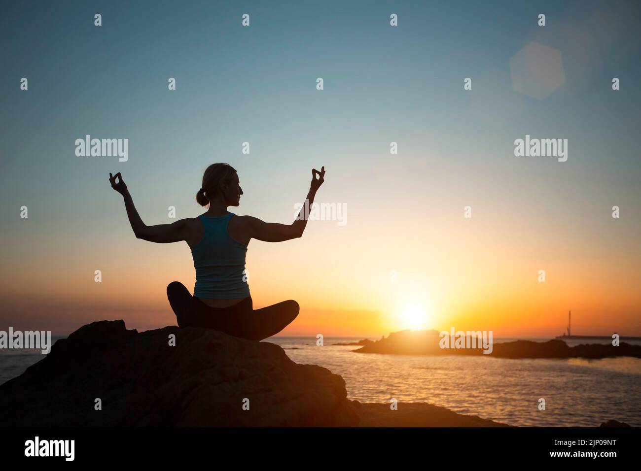 Silhouette donna yoga, meditando sulla spiaggia dell'oceano durante un bellissimo tramonto. Foto Stock