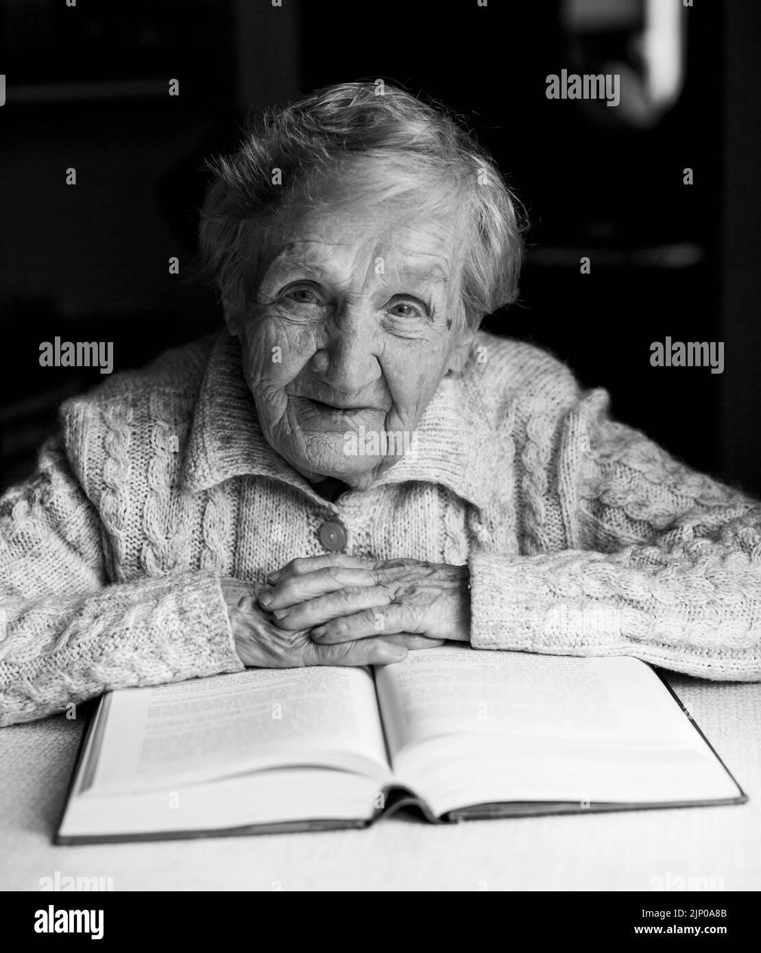 Un ritratto di una vecchia signora che legge un libro nella sua casa. Foto in bianco e nero. Foto Stock