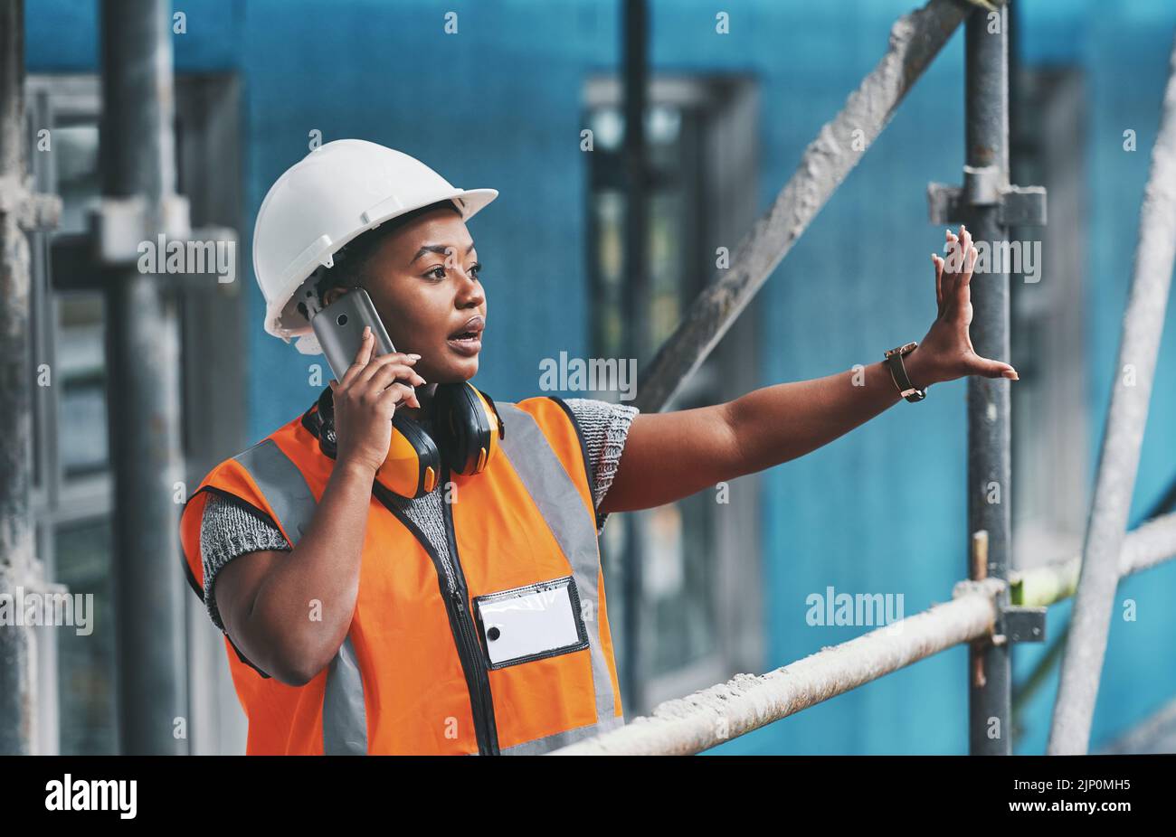 Lavoratore di costruzione che parla durante una telefonata mentre è in piedi in un edificio vuoto. Costruttore professionista che discute i piani e la strategia, controllando il Foto Stock