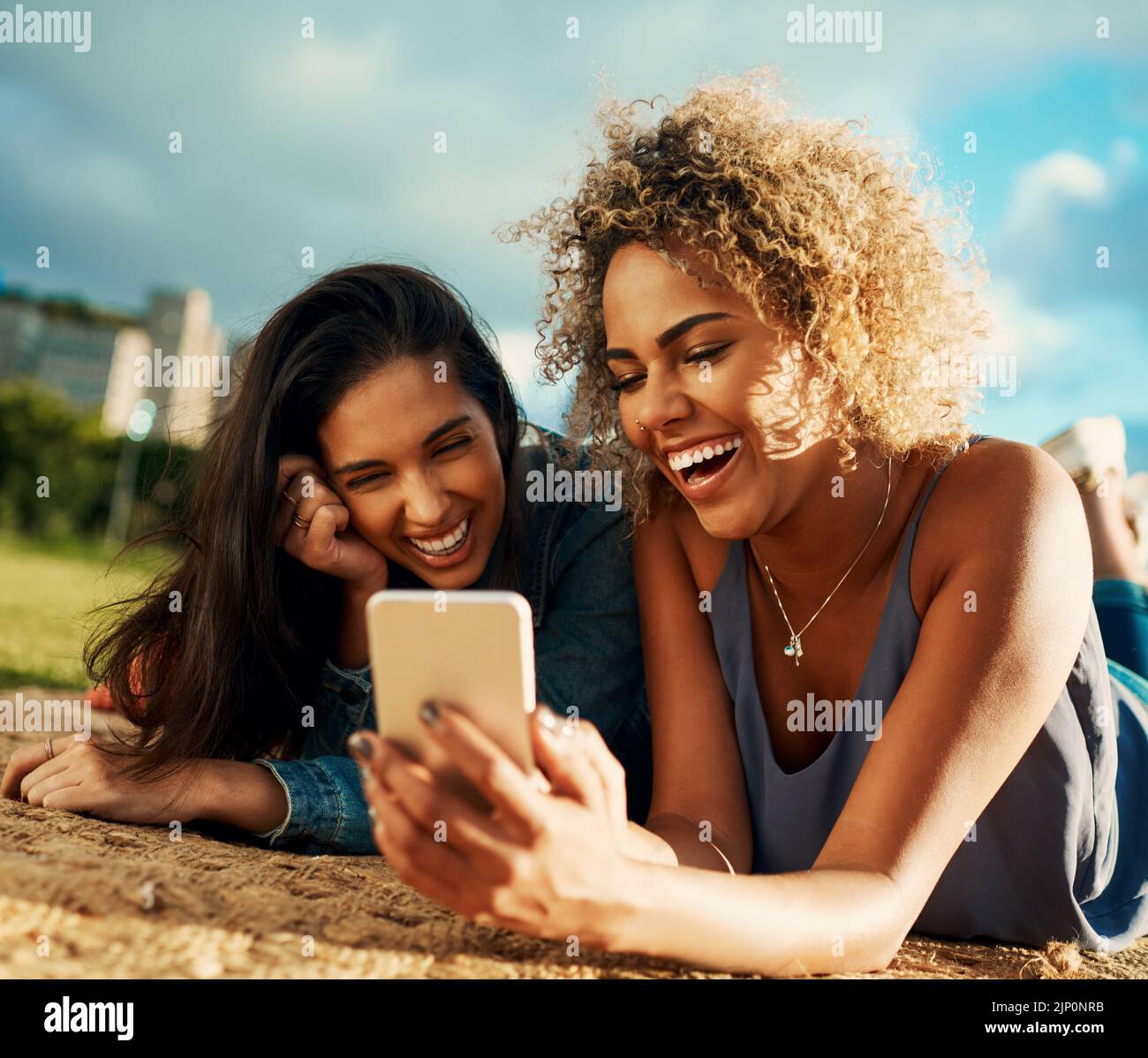 Guarda quanto ti stupida guardare in questa foto. Due giovani simpatico fidanzate che usano uno smartphone insieme mentre sdraiati in un parco. Foto Stock