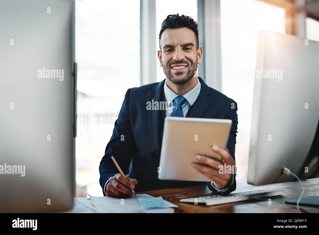Ottenere aiuto dai suoi dispositivi per portare a termine il lavoro. Un bel dirigente maschile che lavora in un ufficio moderno. Foto Stock