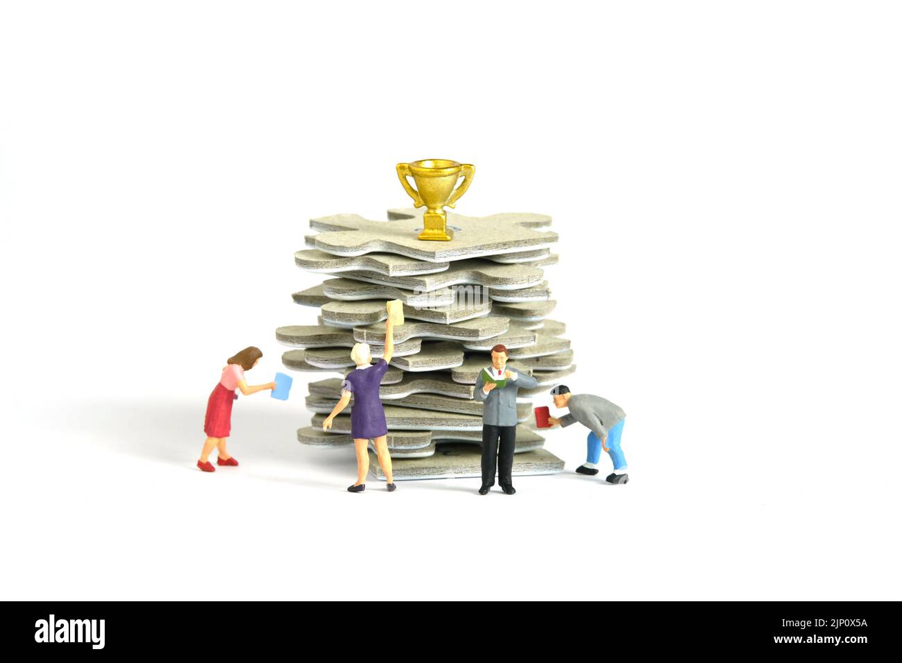 Fotografia di figura giocattolo delle persone in miniatura. Un gruppo di studenti in piedi sopra puzzle jigsaw stack, con trofeo d'oro sopra di esso, isolato su sfondo bianco Foto Stock