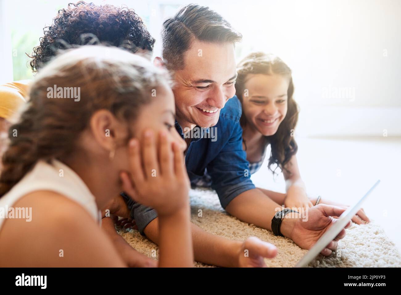 Guarda qui, bambini. Una famiglia di quattro persone che guarda un tablet mentre si siede sul divano di casa. Foto Stock