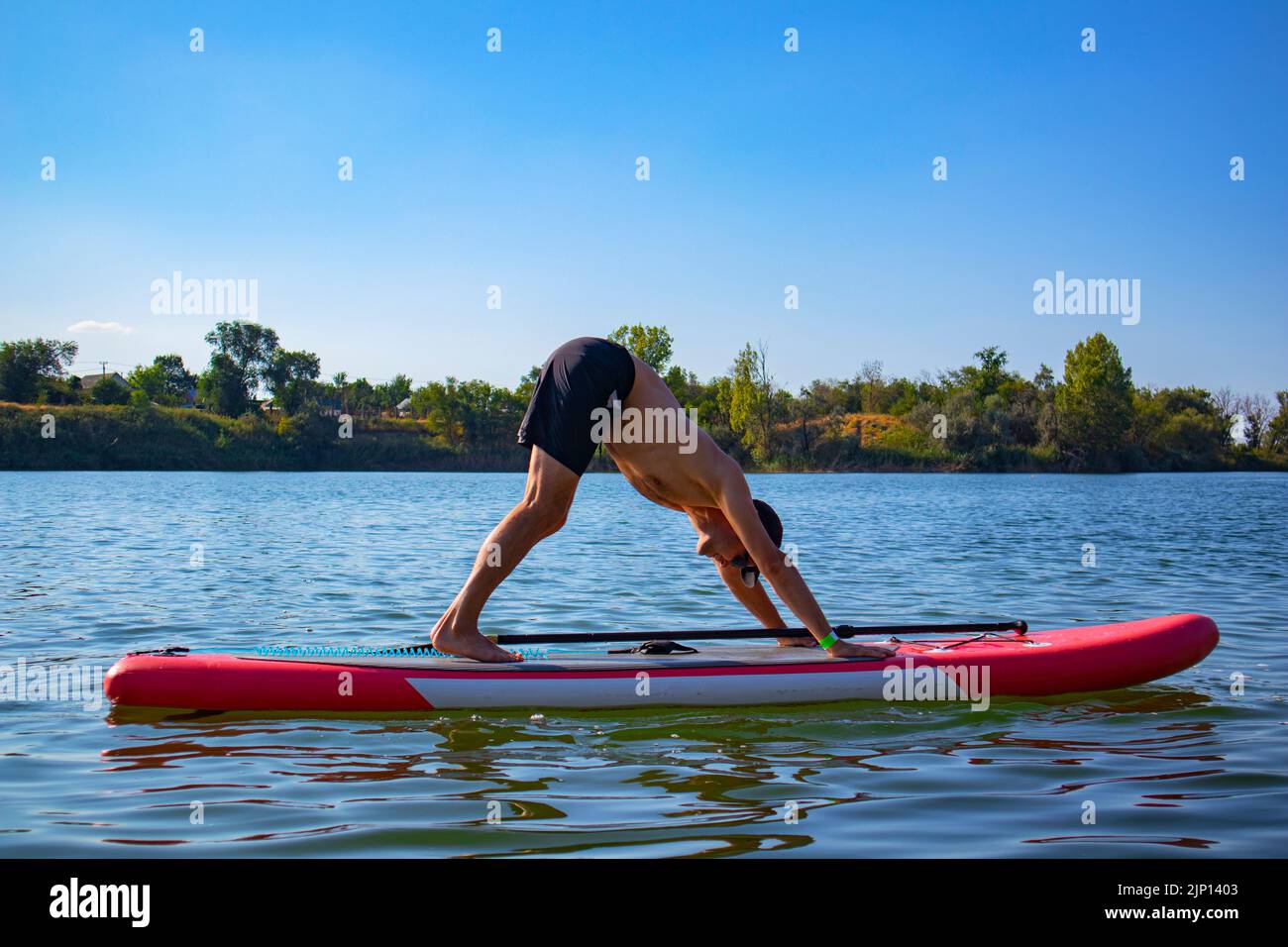 yoga sul bordo del sap. il tipo nel cane posa di faccia giù. sport acquatici. Foto Stock