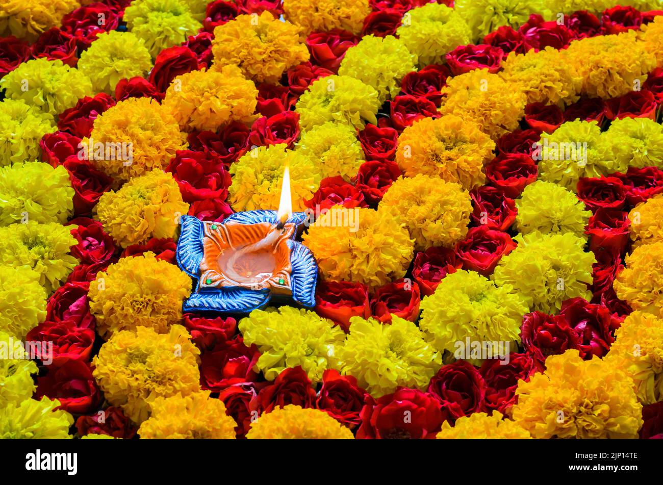 Rangoli decorativi di fiori di rosa e marigold per la festa di Diwali con lampada di diya in argilla accesa con fiamma. Foto Stock